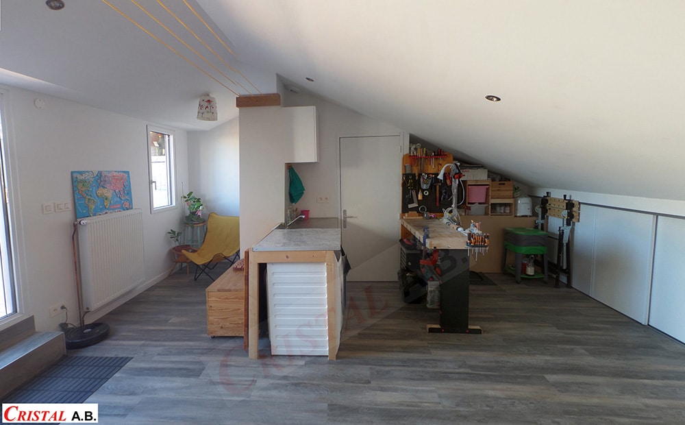 Aménagement de combles avec atelier, coin buanderie et salon sous toit en pente. Logo CRISTAL A.B. visible.
