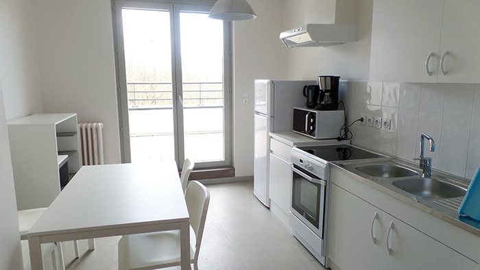 Cuisine moderne blanche avec coin repas, four, micro-ondes, évier et grande porte-fenêtre lumineuse.