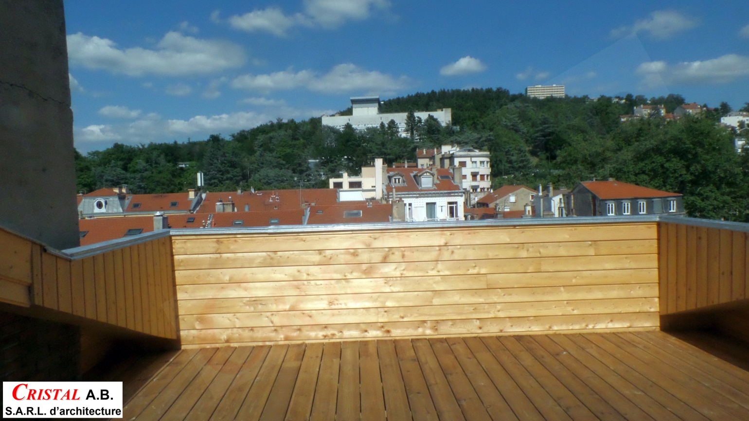 Terrasse en bois par Cristal A.B. Architecture, vue panoramique sur les toits de la ville et une colline arborée.