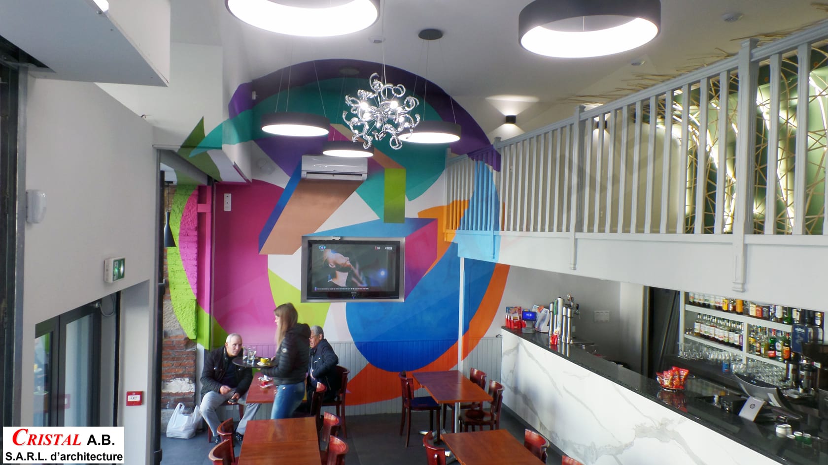 Intérieur moderne du café Cristal A.B. avec fresque géométrique colorée, mobilier en bois et mezzanine architecturale.