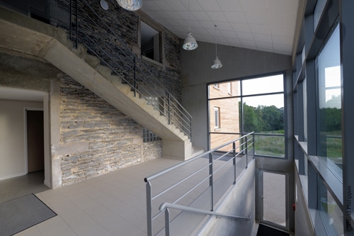 Intérieur moderne avec escalier en béton, mur en pierre apparente et baies vitrées. Photo par David Phillippon.