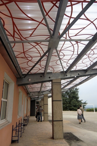 Auvent moderne à motifs rouges sur structure métallique couvrant un passage piéton extérieur avec piliers en béton.