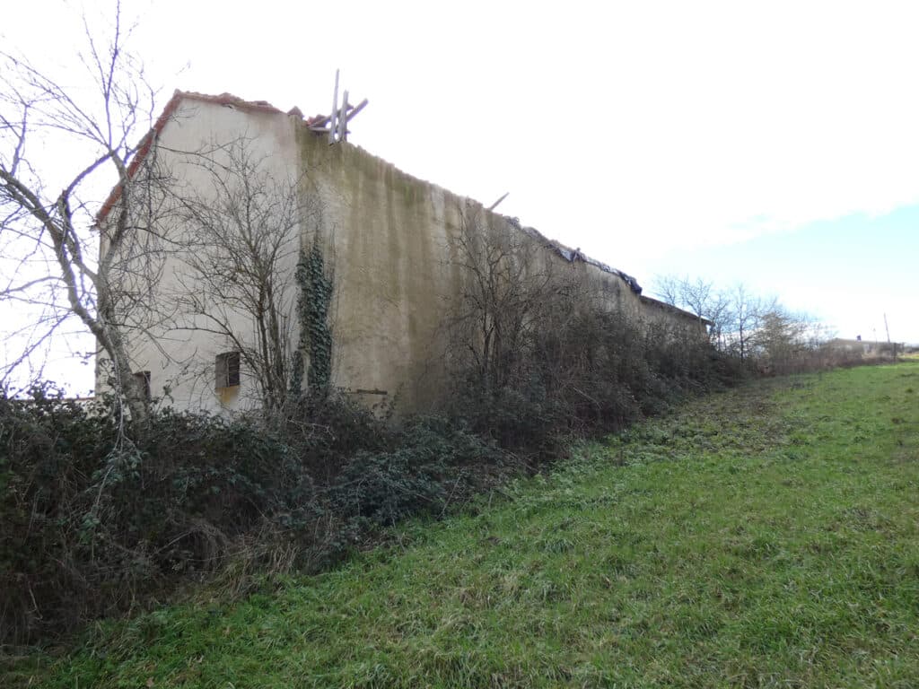 Ancienne grange délabrée avec toit effondré et végétation sauvage sur une colline herbeuse.