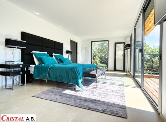 Chambre contemporaine avec lit sarcelle, grande tête de lit noire, tapis gris et baie vitrée. Logo Cristal A.B.