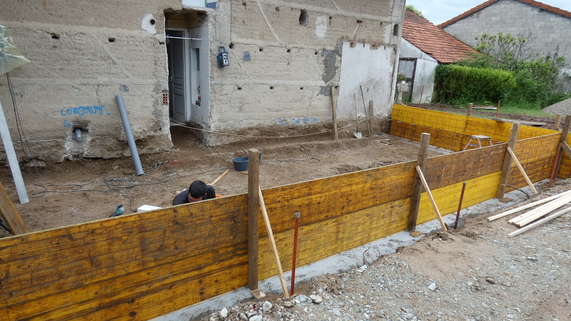 Ouvrier installant un coffrage en bois pour une extension de maison sur une dalle en béton.
