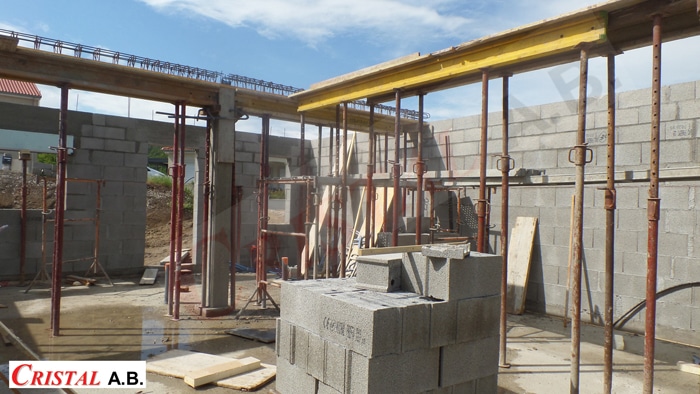 Chantier de maçonnerie avec murs en parpaings, étais métalliques et coffrage. Logo Cristal A.B. visible.