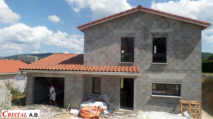 Maison en parpaings avec toit en tuiles rouges en chantier par CRISTAL A.B. avec ouvrier et matériaux.
