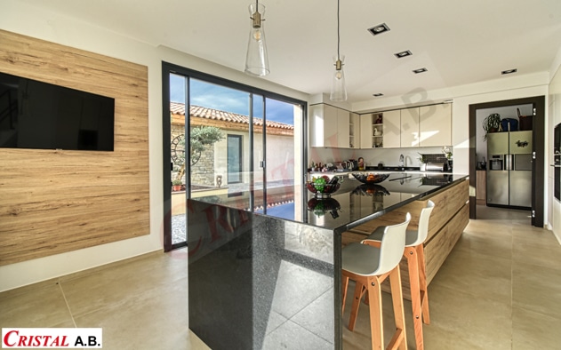 Cuisine moderne avec îlot en granit noir, meubles en bois et vue sur le patio par Cristal A.B.