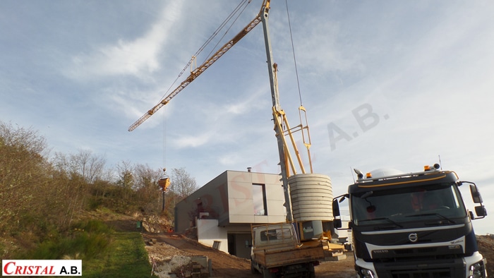 Grue de chantier Cristal A.B. levant une charge près d'une maison moderne et d'un camion Volvo.