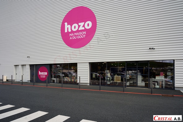 Devanture du magasin Hozo avec logo rose hozo MA MAISON A DU GOÛT sur mur métallique gris et vitrines.