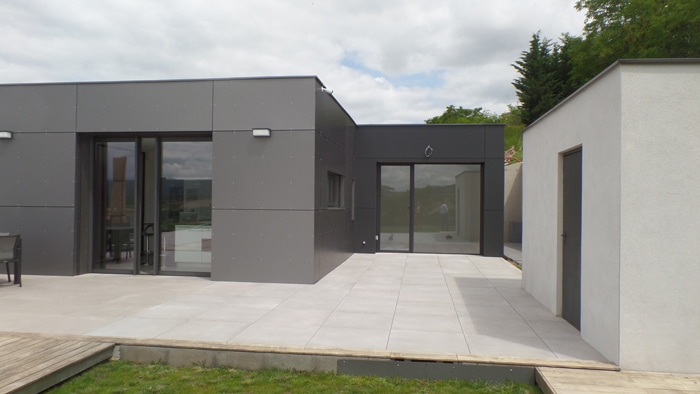 Maison contemporaine à façade grise avec grande terrasse en dalles et baies vitrées coulissantes.