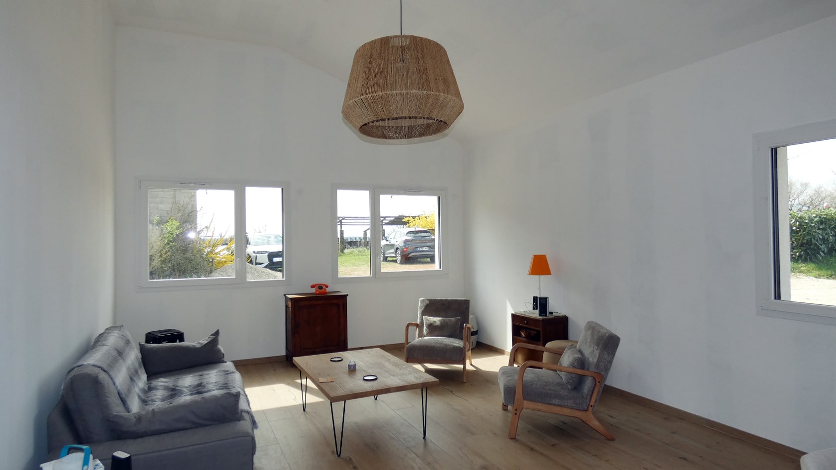Salon moderne et lumineux avec canapé gris, table basse en bois et suspension en osier tressé.