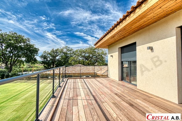 Terrasse moderne en bois et garde-corps avec vue sur jardin verdoyant et ciel bleu. Logo Cristal A.B.