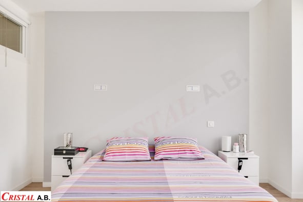 Chambre moderne avec lit, couette rayée colorée 'colour is beautiful', tables de chevet blanches et mur gris clair.