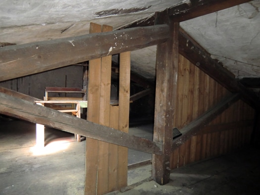 Vieux grenier avec charpente en bois massif, poutres apparentes et établi rustique sous un toit incliné.