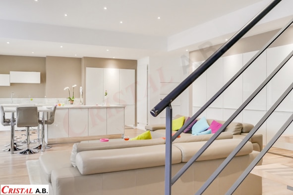 Salon moderne lumineux avec canapé beige, coussins colorés et cuisine ouverte. Logo CRISTAL A.B.