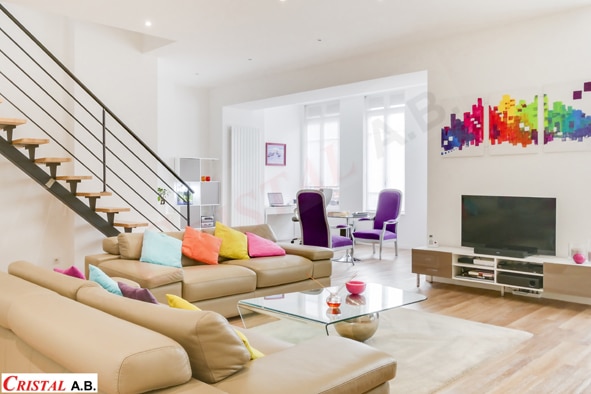 Salon moderne avec canapés en cuir, coussins colorés, escalier design et coin bureau. Cristal A.B.